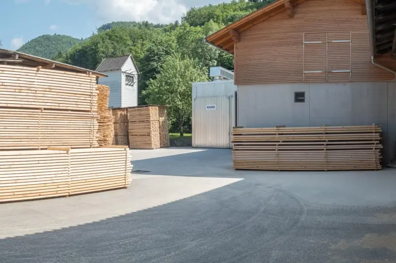Betriebshof des Sägewerks mit luftgetrockneten Schnittholzstapeln und Trockenkammer